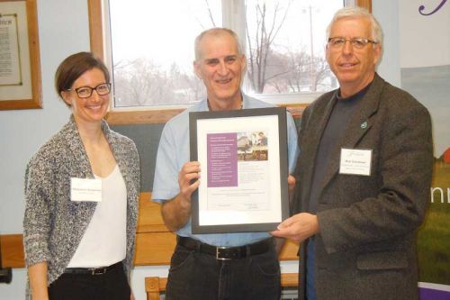 Deputy warden/mayor of South Frontenac, Ron Vandewal, presents Stephanie Sciberras and Ross Sutherland with a community partnership plaque
